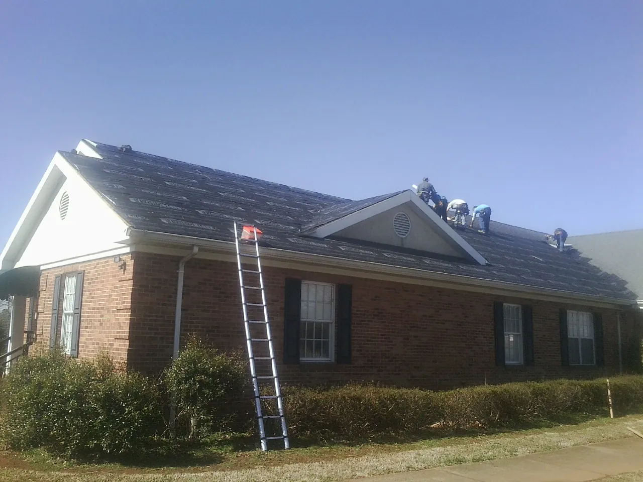 Crew tearing shingles off a brick ranch roof with a ladder set — Metal Roof Repair work by our crew in Kimball