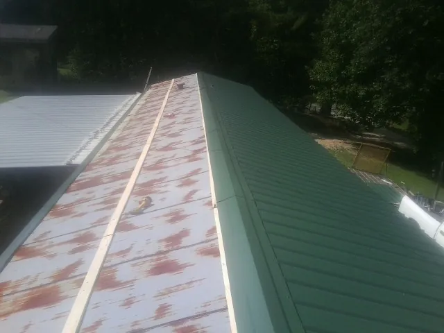 Old rusted panels beside newly installed green metal roofing — Wind Damage Roof Repair by Roofing Brothers in Kimball