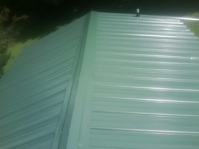 New green metal panels meeting at the ridge of a roof — Flat Roof Repair work by our crew in Kimball