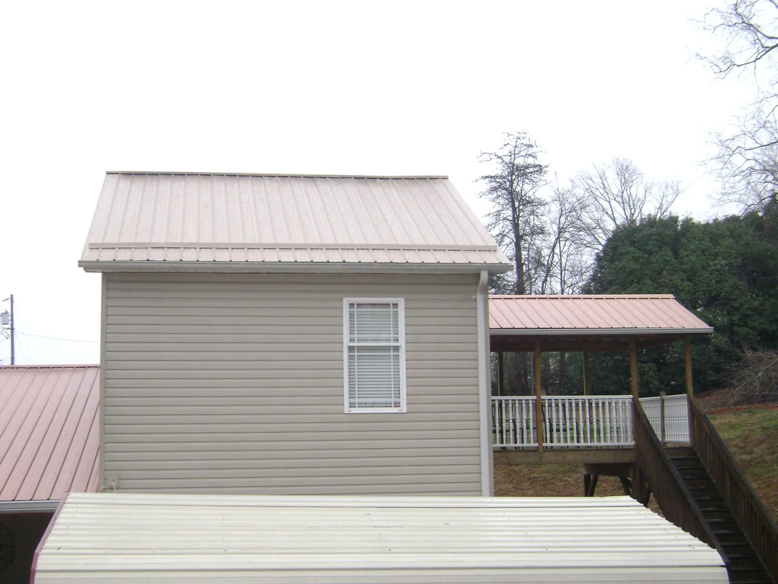 Tan metal roofs on a two story addition and attached porch, from a Roof Replacement job in Kimball